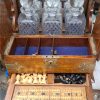 Antique Victorian Games Tantalus With Three Cut Glass Decanters. Oak with brass corner fixings and decorative work. Mirrored back. The front opens up to reveal games pieces. The Tantalus was presented to E. Ainsworth in September 1899 as 1st Prize in the Leamington Spar Bowls Club Handicap. The item measures 35cm by 32cm by 22cm.